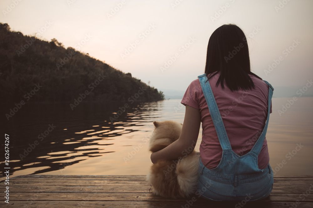 Woman sit and relax with her dog admire the sunset sky and the lake.
