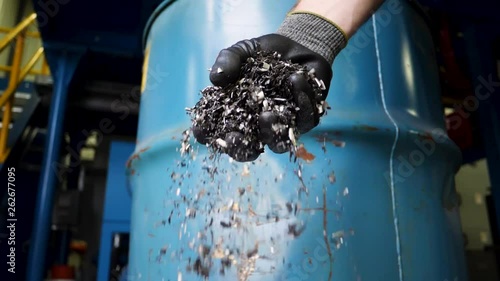 Gloved hand drops metal turnings into a bucket photo