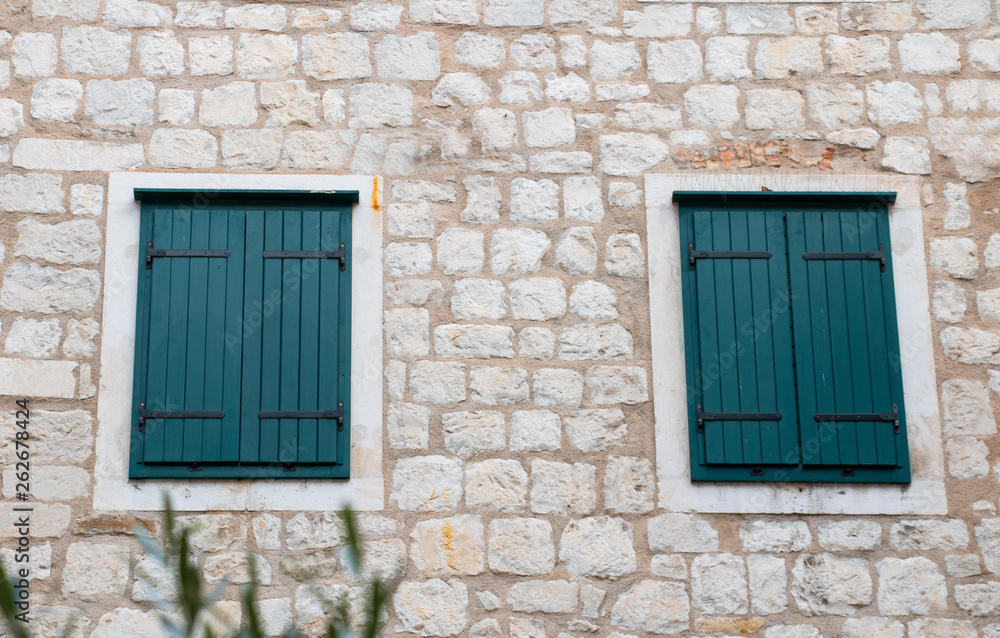 the stone wall of the house is light with shuttered windows