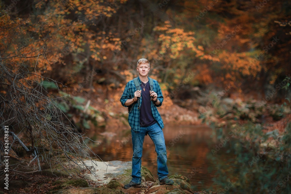 Redhead man in a plaid shirt and purple t-shirt stands on the coast of a mountain stream in the autumn forest near  in the Grand Canyon of Crimea. Autumn, travel and hiking concept.