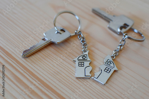 Pendant of key ring in shape of house divided in two parts on wooden background, closeup view. Dividing house when divorce, division of property and real estate.