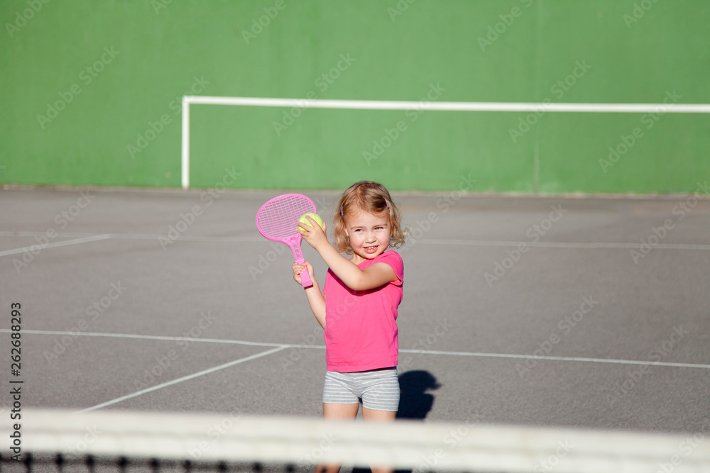 Kid is playing tennis on court. Cute child is having fun playing sports activities outdoors. Little girl has practice in summer game.