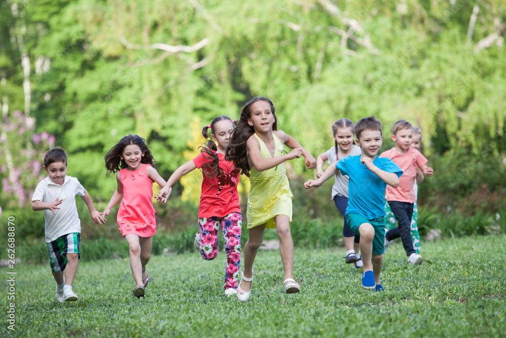 A group of happy children of boys and girls run in the Park on the grass on a Sunny summer day . The concept of ethnic friendship, peace, kindness, childhood.