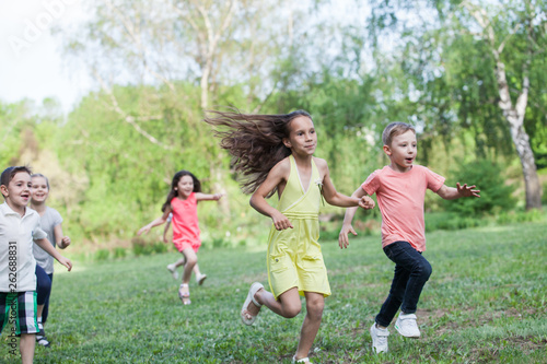 A group of happy children of boys and girls run in the Park on the grass on a Sunny summer day . The concept of ethnic friendship, peace, kindness, childhood.