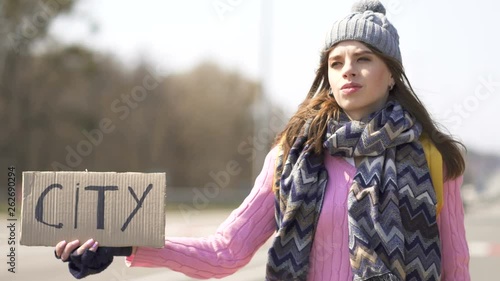 Young woman hitchhiking  try to get city with poster . Voyager team photo