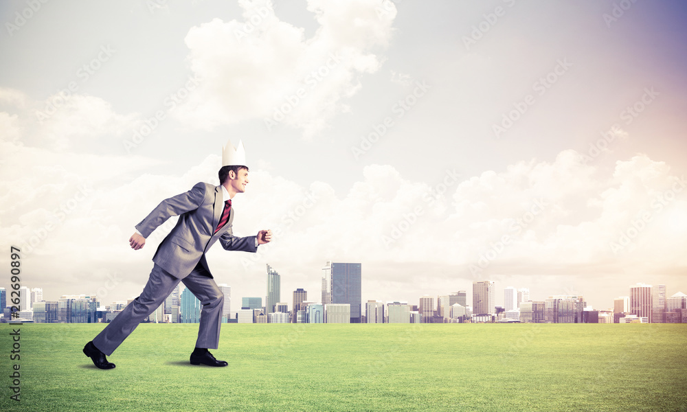 King businessman in elegant suit running on green grass and modern cityscape at background King businessman in elegant suit running on green grass and modern cityscape at background