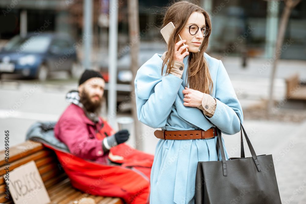 Homeless begging money while sitting on the bench with passing by businesswoman near the business center Homeless begging money while sitting on the bench with passing by businesswoman near the business center