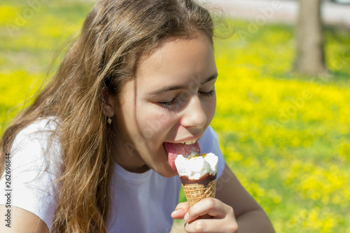 Beautiful teen girl eating ice cream in a waffle cone in summer. Selective focus