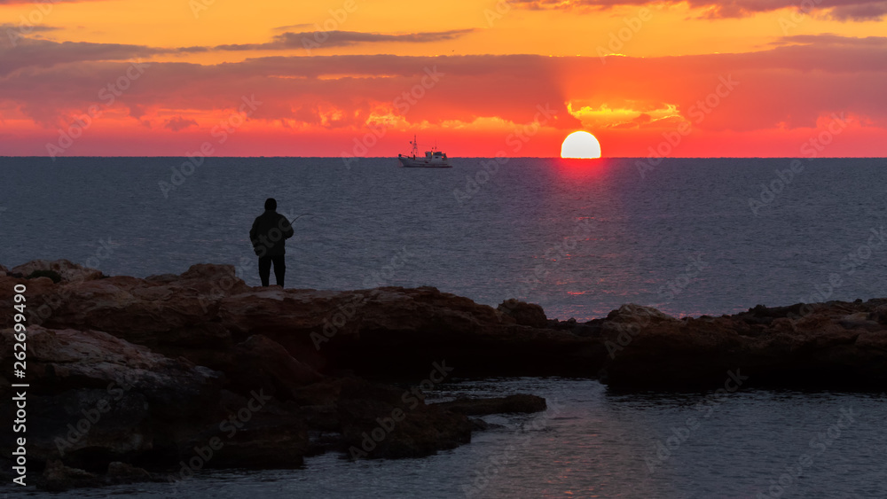 An angler fishes in the Mediterranean on the rocky coast at Torrevieja in the morning at sunrise