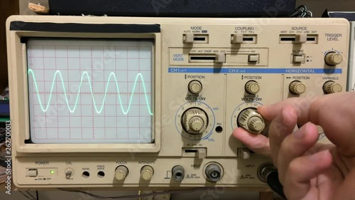 Electronics working with oscilloscope and sine wave shown on oscilloscope
