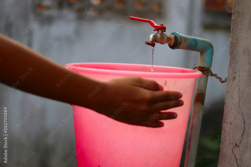 Young hands collecting water with a plastic bucket from an old slow