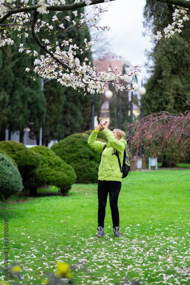 A beautiful blonde woman photographs trees against a green park