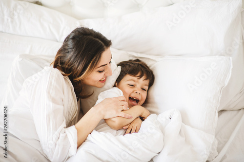 Young mother with her little son relaxing and playing in the bed at the weekend together