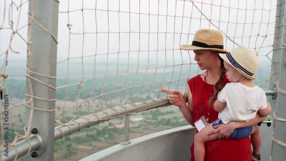 Young mother is showing her son something on the ground from helium air balloon in Cambodia, touristic attraction allowing to see Angkor temples complex from above Young mother is showing her son something on the ground from helium air balloon in Cambodia, touristic attraction allowing to see Angkor temples complex from above
