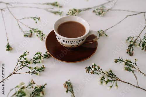 A cup of coffee in a frame of flowers and branches on white background. Flat lay, top view, copy space. 