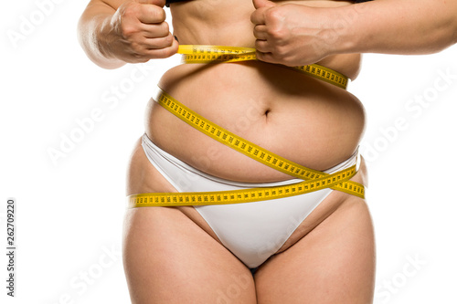 a fat woman measuring her belly on white background