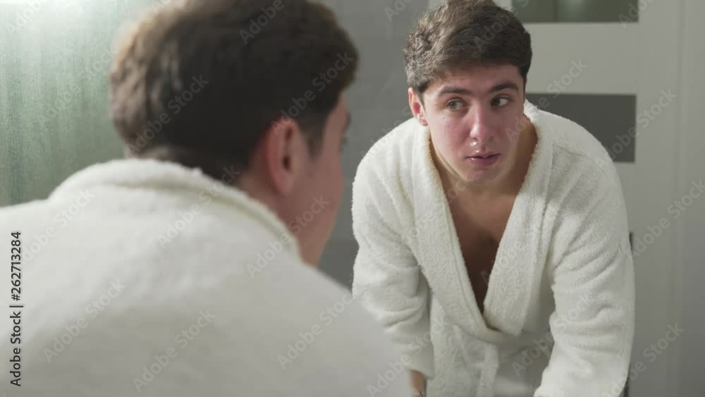 Handsome man is washing his face from shaving foam. Back view. Looking in the mirror. Handsome man is washing his face from shaving foam. Back view. Looking in the mirror.