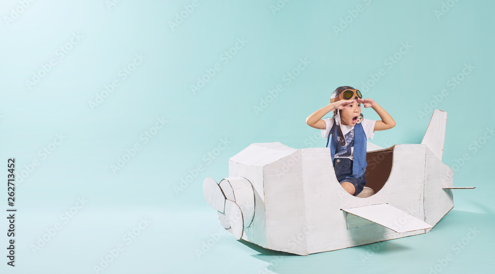 Little cute girl playing with a cardboard airplane. White retro style cardboard airplane on mint green background . Childhood dream imagination concept . Horizontal format .