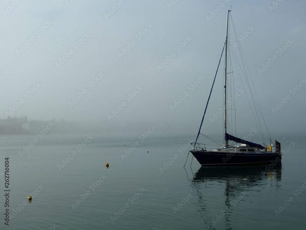 Boat anchored in harbour on a foggy day in Skerries, Dublin. Boat sail reflected in the water. 