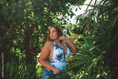 Overweight girl  beautiful young girl in a white one-piece swimsuit and in jeans shorts in tropical plants posing .portrait  horizontal image                                                           Google                                       