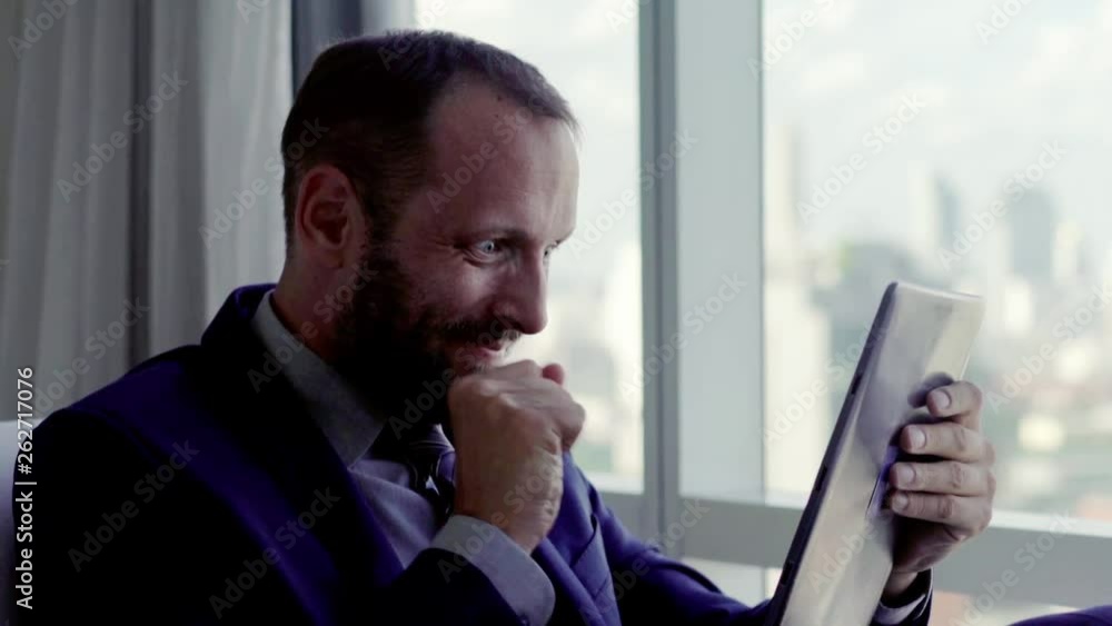 Happy businessman reading good news on tablet computer sitting on armchair at home Happy businessman reading good news on tablet computer sitting on armchair at home