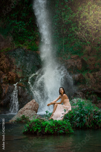 Fototapeta Naklejka Na Ścianę i Meble -  Sexy woman posing on the rock among green tropical plants and beside beautiful waterfall with blue water. Fairy tale.