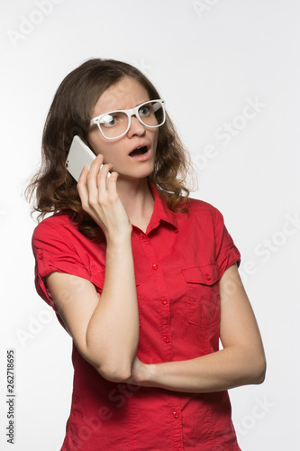 Beautiful girl in glasses in surprise opened her mouth talking on the phone on a white background
