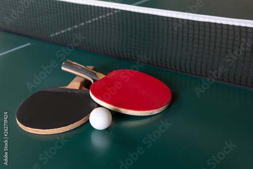 two ping-pong rackets and a ball on a green table. ping-pong net.