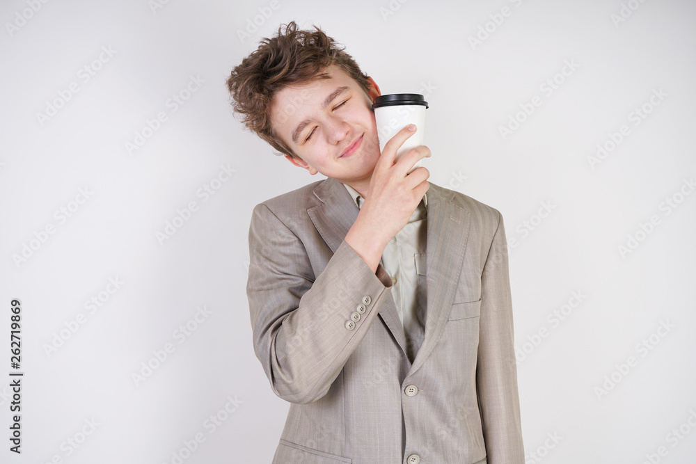 tired teen boy in grey business suit with paper Cup of coffee in hand on white studio background tired teen boy in grey business suit with paper Cup of coffee in hand on white studio background