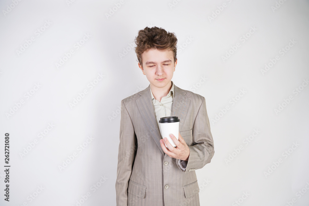 tired teen boy in grey business suit with paper Cup of coffee in hand on white studio background tired teen boy in grey business suit with paper Cup of coffee in hand on white studio background