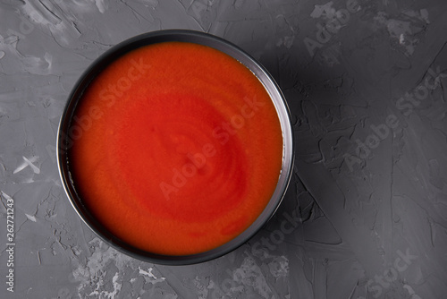 Tomato soup in a black plate on a gray concrete background without entourage