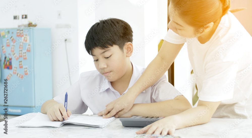 Asian mother helping her son doing homework on white table. Asian mother helping her son doing homework on white table.