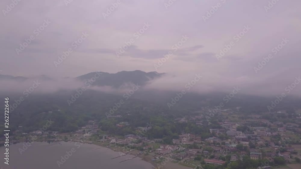 Aerial drone slowly panning above a coastal town filled with little houses and buildings surrounded by lush green forest on an overcast cloudy afternoon with grey skies Aerial drone slowly panning above a coastal town filled with little houses and buildings surrounded by lush green forest on an overcast cloudy afternoon with grey skies