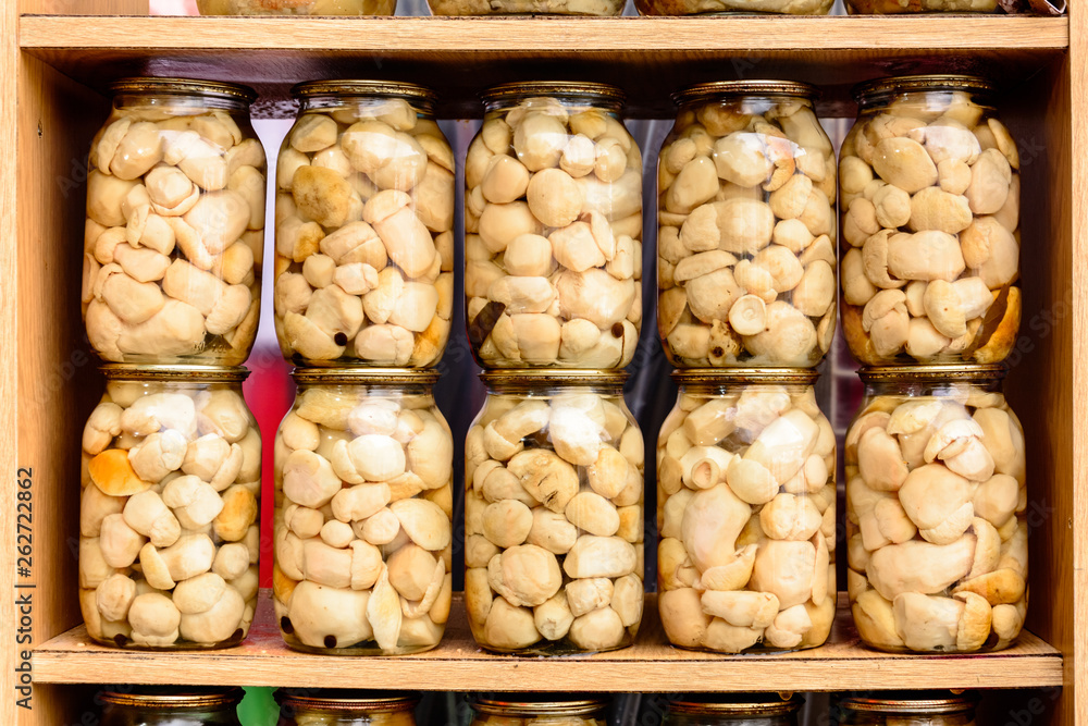 Delicious delicious white marinated mushrooms in glass jars on shelves.
