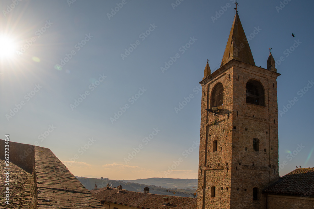 Back light view with lens flare of a medieval bell tower in the ancient village of Serralunga d'Alba with the Langhe hills in the background in springtime, Piedmont, Italy