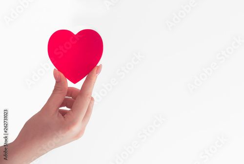 female hand holds red heart in fingers, red big paper heart, give love, white background, place for text
