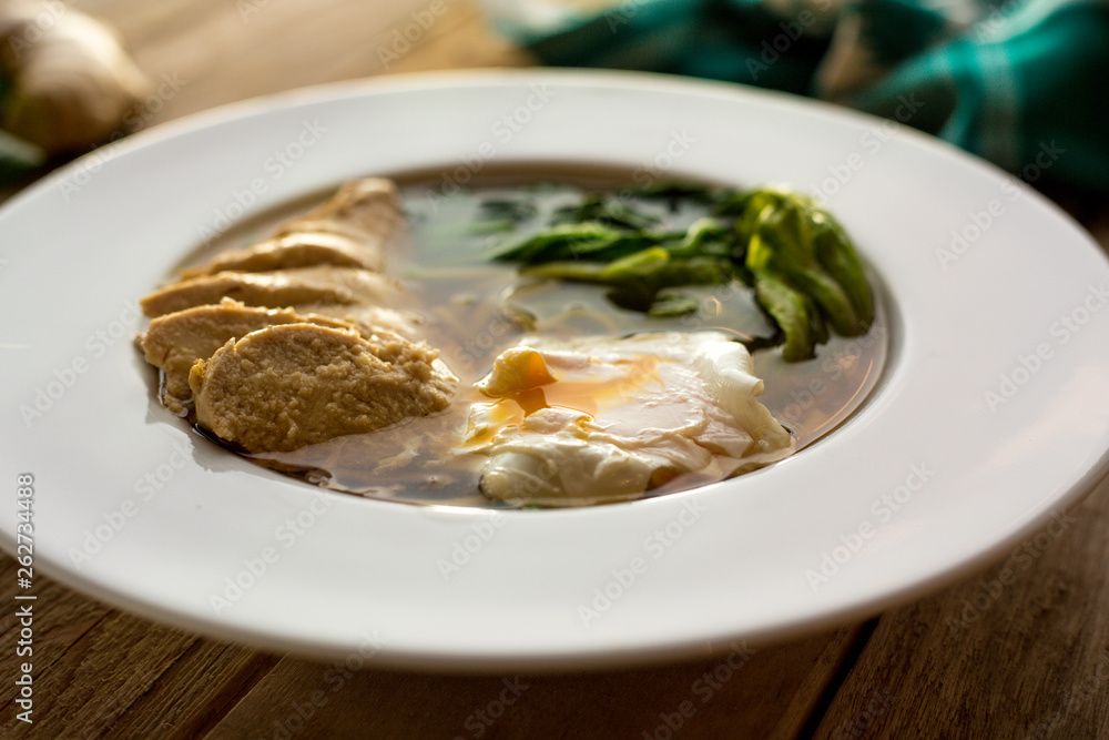 Homemade soup with poached egg, boiled chicken and spinach. On wooden table. Ginger. Garlic. Ingredients. Homemade. Homemade soup with poached egg, boiled chicken and spinach. On wooden table. Ginger. Garlic. Ingredients. Homemade.