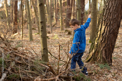 A boy in a blue jacket sneaks through thickets in the forest, profile view, trees at the edge of the forest