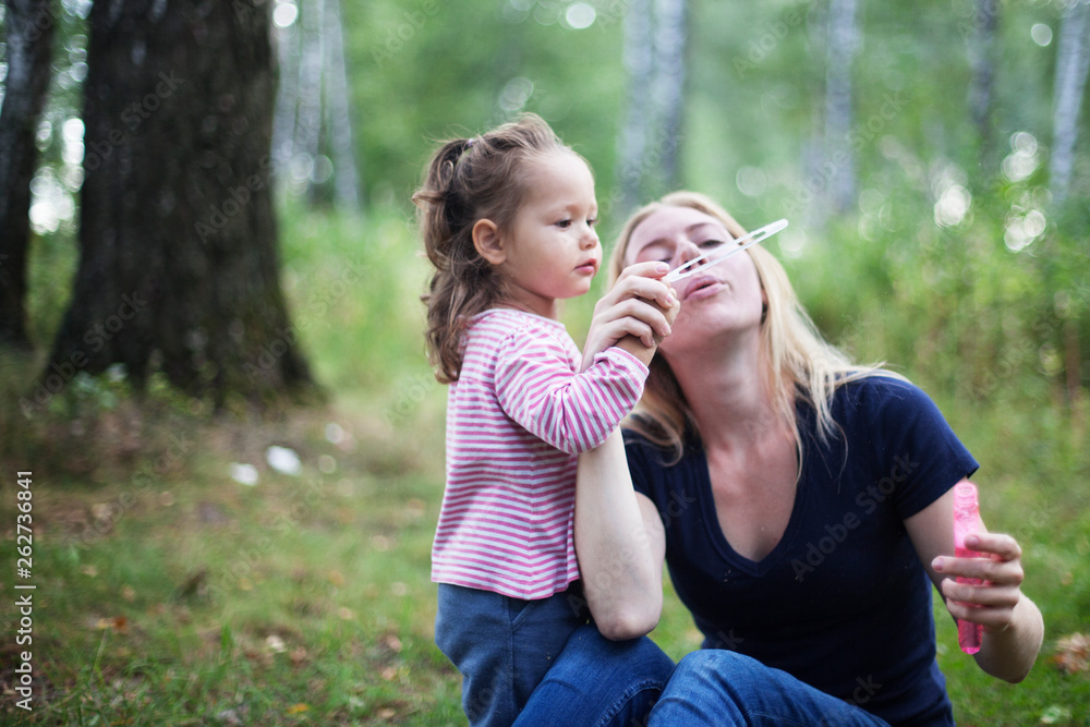 Mother and little daughter blowing soap bubbles in park. Happy and carefree childhood. Good family relations. Mother and little daughter blowing soap bubbles in park. Happy and carefree childhood. Good family relations.