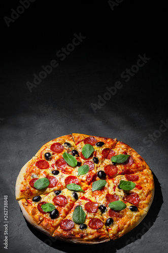 Pepperoni Pizza with Mozzarella cheese, salami, olive, pepper, Spices and Fresh spinach. Italian pizza on Dark grey black slate background