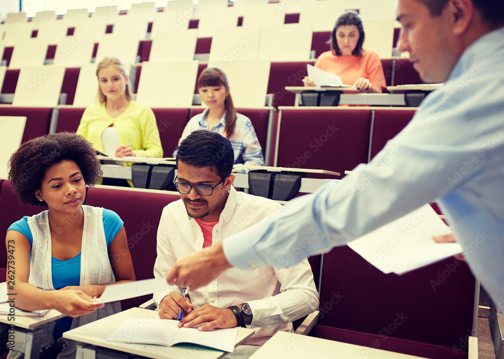 education, high school, university, learning and people concept - teacher giving tests to students at lecture education, high school, university, learning and people concept - teacher giving tests to students at lecture