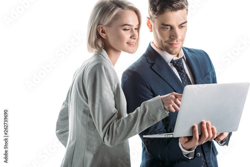 cheerful businesswoman pointing with finger at laptop screen near handsome businessman isolated on white