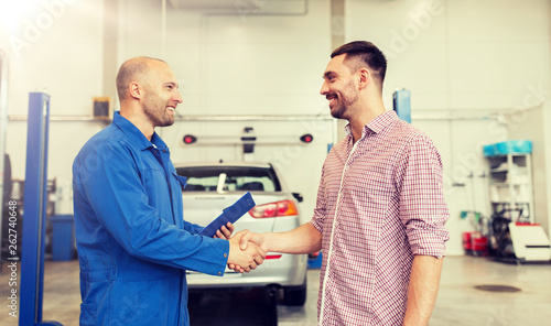 auto service  repair  maintenance  gesture and people concept - mechanic with clipboard and man or owner shaking hands at car shop