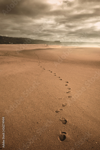 Lonely human footprints on a wide sandy beach in cloudy weather in the city of Nazare in Portugal