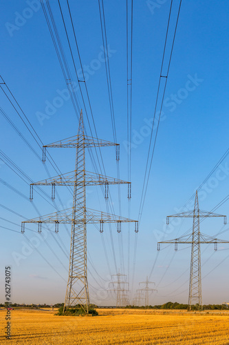 Hochspannungsleitung gespannt zwischen Strommasten bei strahlend blauem Himmel, Hochformat