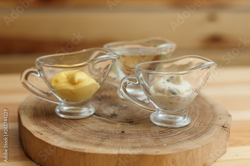 Set of three transparent sauceboats with different sauces on wooden plate