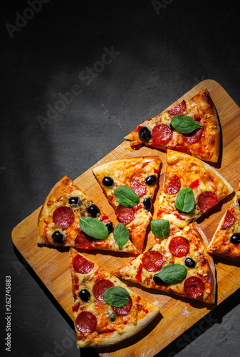 Pepperoni Pizza with Mozzarella cheese, salami, olive, pepper, Spices and Fresh spinach. Italian pizza on Dark grey black slate background