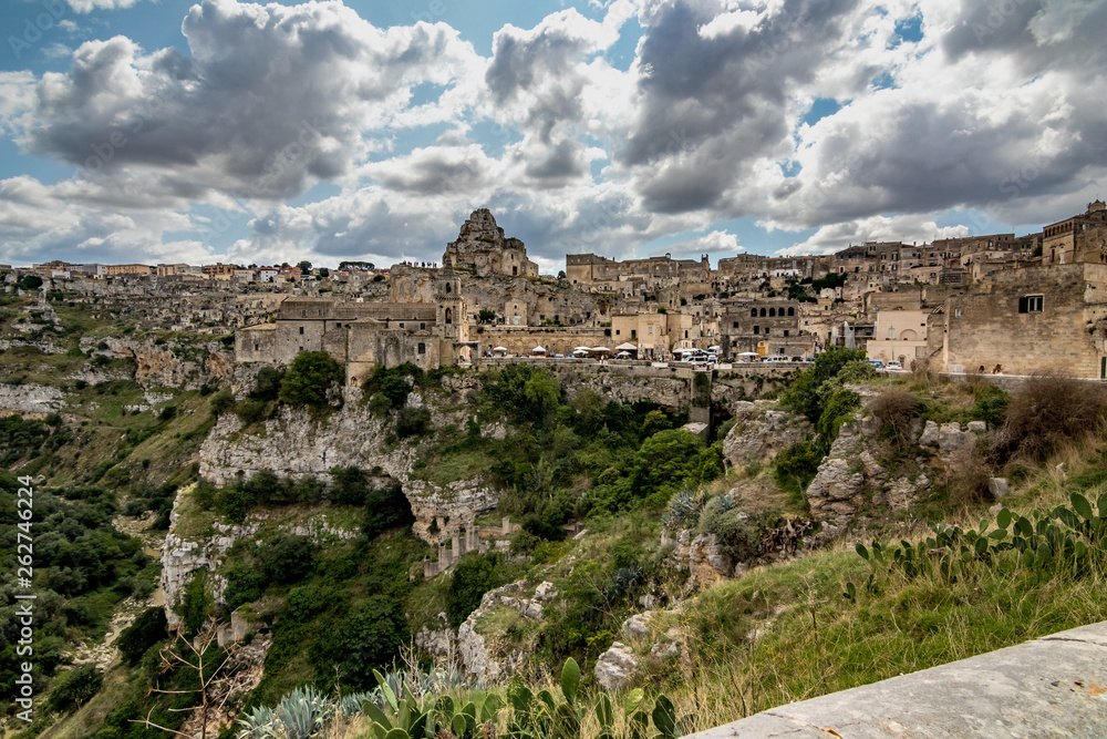 Summer day scenery street view of the amazing ancient town of the Sassi with white puffy clouds moving on the Italian blue sky. Matera, Basilicata, Italy