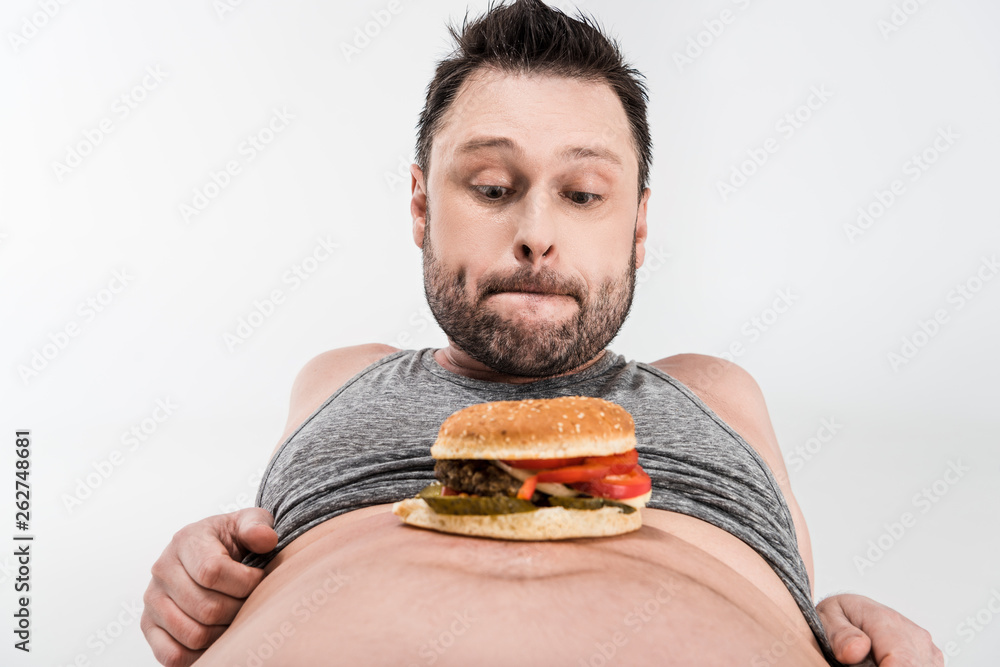 overweight man looking at burger on belly isolated on white overweight man looking at burger on belly isolated on white