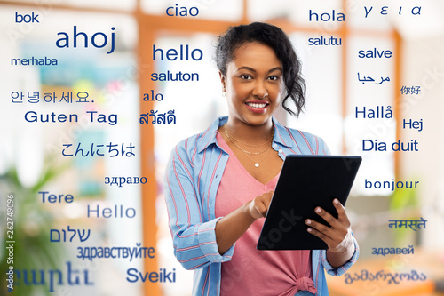 technology, translation and people concept - happy african american woman using tablet computer over greeting words in different foreign languages photo